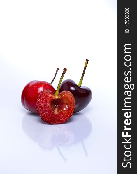 One cut fresh cherry against two whole fresh cherries isolated on white background with reflection in foreground. One cut fresh cherry against two whole fresh cherries isolated on white background with reflection in foreground.