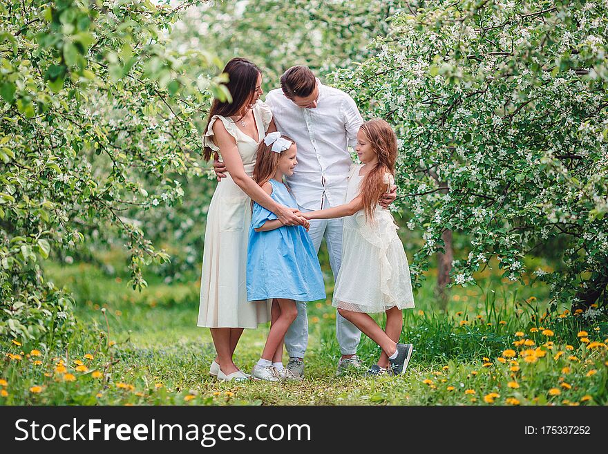 Adorable Family In Blooming Cherry Garden On Beautiful Spring Day