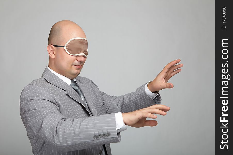 Bald businessman in a gray suit with a gray background with a bandage to sleep in his eyes