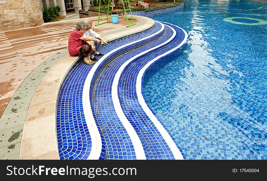 A senior couple sitting beside a pool