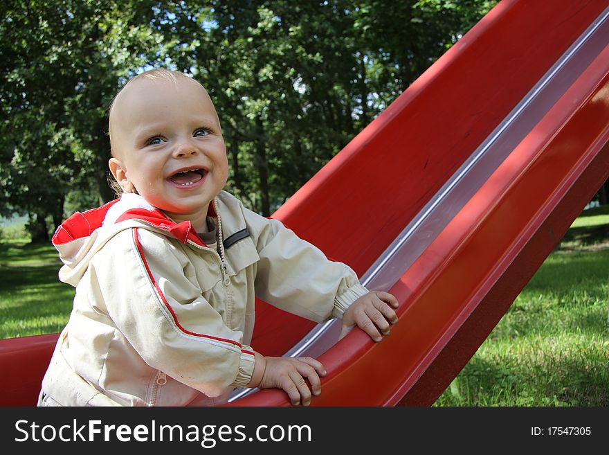 Happy baby on the red slide in a park. Happy baby on the red slide in a park