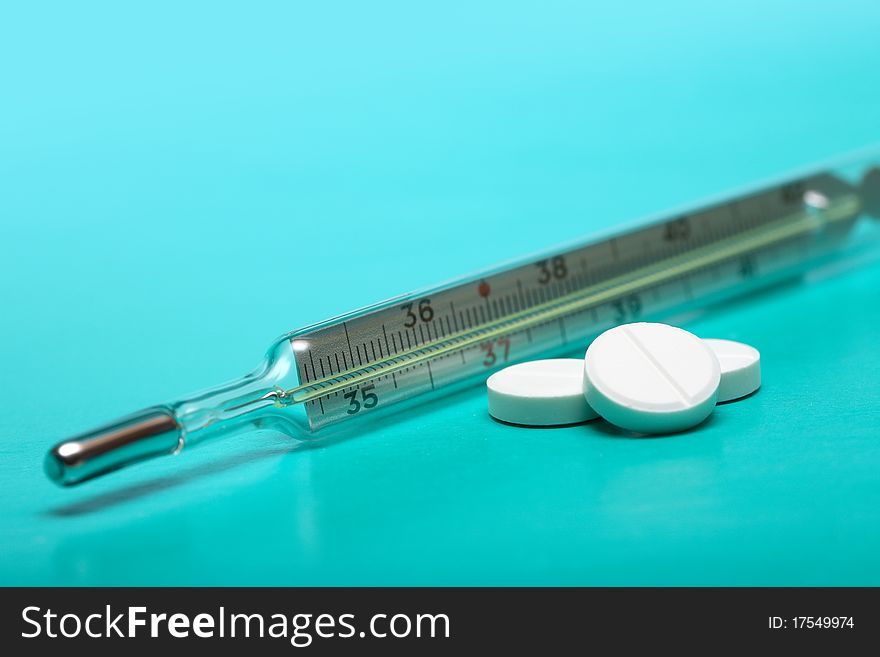 Stack of pills near clinical thermometer on green background. Stack of pills near clinical thermometer on green background