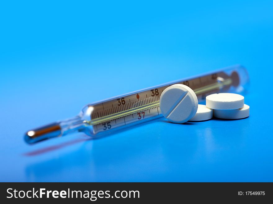 Stack of pills near clinical thermometer on blue background. Stack of pills near clinical thermometer on blue background