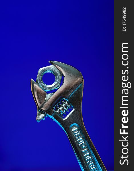 Extreme closeup of adjustable wrench gripping a nut on blue background. Extreme closeup of adjustable wrench gripping a nut on blue background