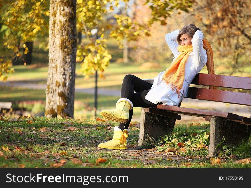 Young woman sitting on bench in park and tying her scarf