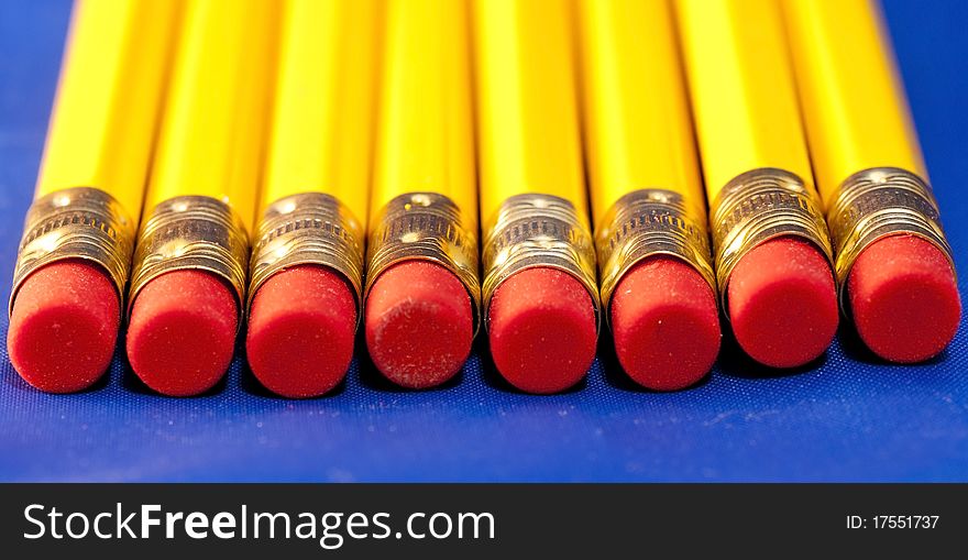Line of yellow pencils with red rubbers against the blue background. Line of yellow pencils with red rubbers against the blue background