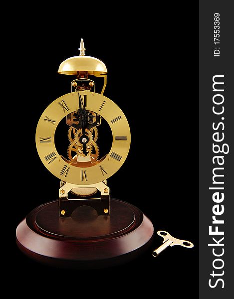 An old-fashioned, gold colored, windup clock with its key.  Isolated on black. An old-fashioned, gold colored, windup clock with its key.  Isolated on black.