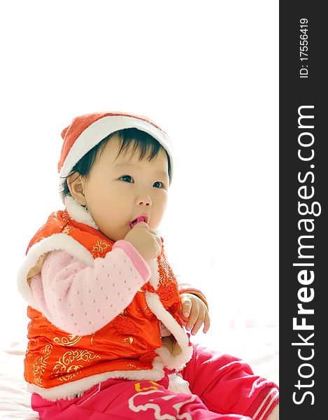 A Asian baby girl sitting on the bed，who Wearing a Christmas hat