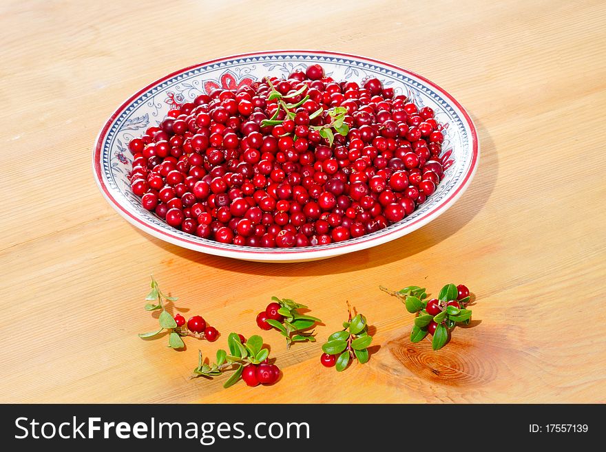 Fresh cranberries on a plate on a wooden table.