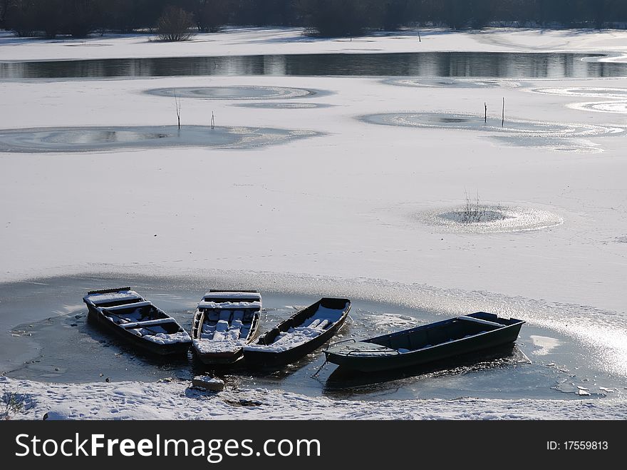 Winter landscape. Small frozen river and boats  on ice