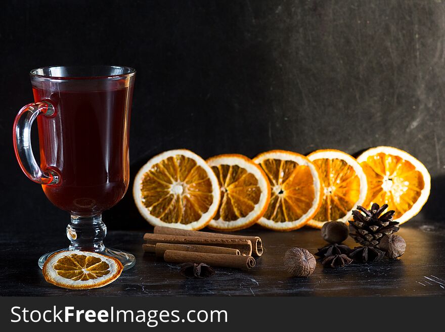Glass cup of mulled wine, spices and pieces of oranges on the black background
