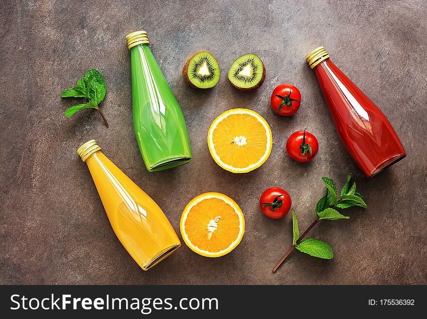 Flat Lay A Variety Of Bottled Juices And Halves Of Fruits And Vegetables On A Dark Rustic Background. Assorted Juices, Tomato,