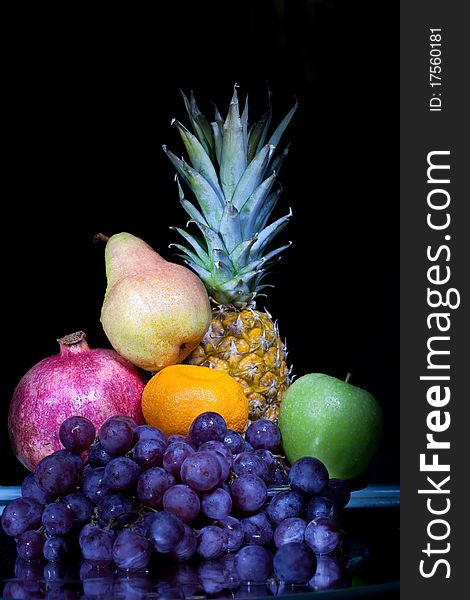 Fruit: pineapple, grapes, a tangerine, a pomegranate, a green apple against a dark background. Fruit: pineapple, grapes, a tangerine, a pomegranate, a green apple against a dark background