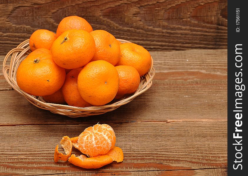 Ripe tangerine fruits in basket on wood background