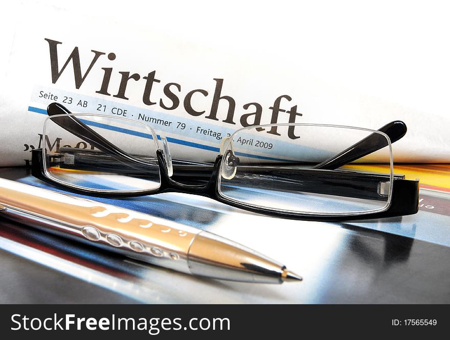 Newspaper with lettering Economy in German language plus glasses an ball point. Newspaper with lettering Economy in German language plus glasses an ball point