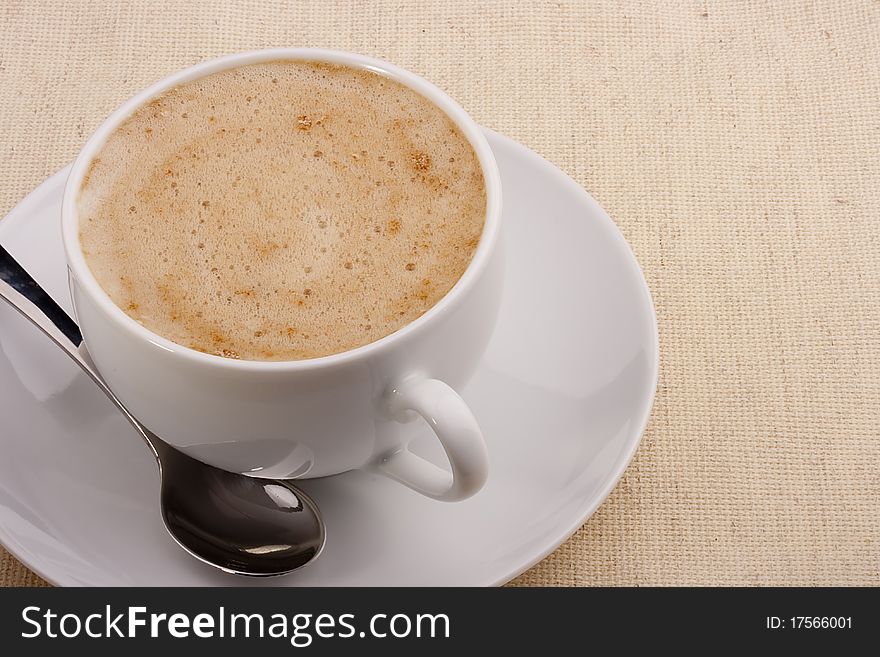 Cappuccino in a white ceramic cup with a saucer and a spoon.