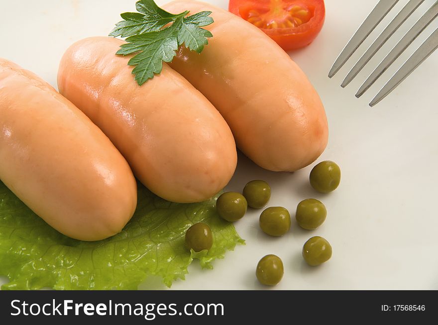 Three Small sausages decorated with green lettuce and tomato