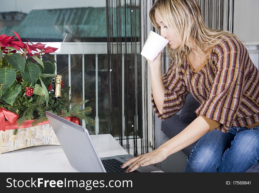 Happy blond woman on her couch working on her laptop and taking a sip from her coffee. Happy blond woman on her couch working on her laptop and taking a sip from her coffee