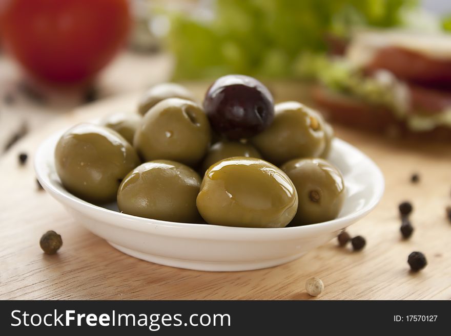 Green olives in a bowl on  a wooden board.