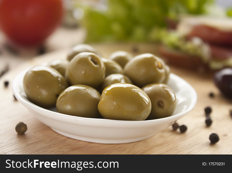 Green olives in a bowl on a wooden board.