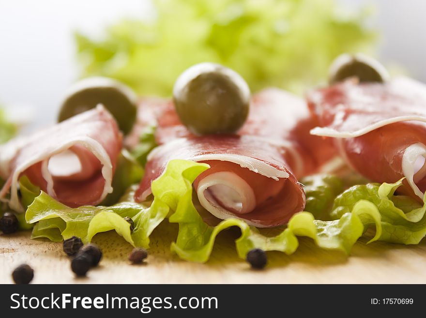 Slices of prosciutto rolled up and arranged on a lettuce leaf. Shallow depth of field.