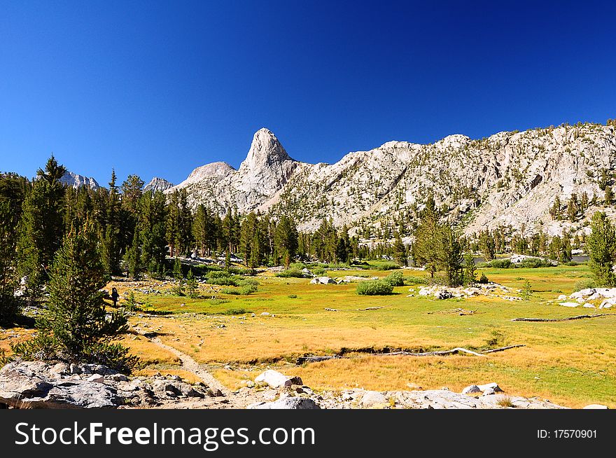 I green grassy meadow found below a mountainous wall. I green grassy meadow found below a mountainous wall