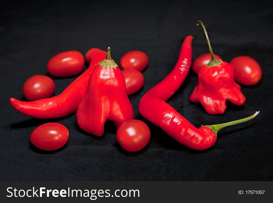 Red hot chilli peppers and cherry tomatoes isolated on a black background.