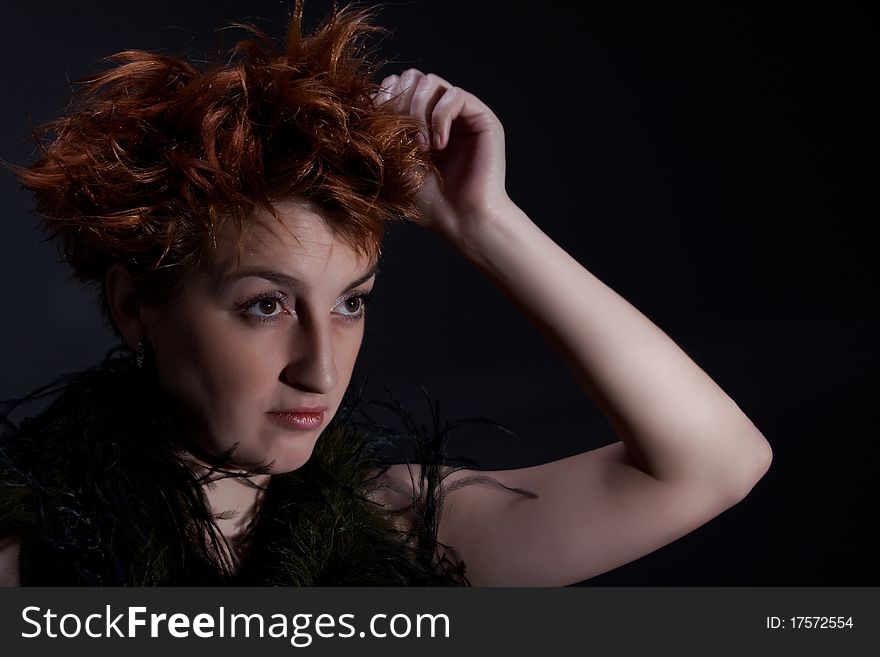 Portrait the red girl against a dark background dressed in a boa