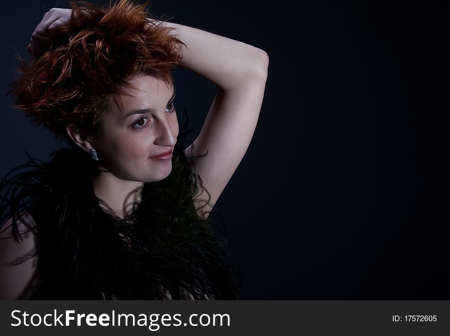 Portrait the red girl against a dark background dressed in a boa