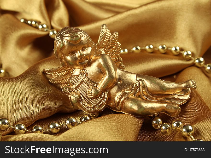 Little gold angel with a harp lying on the golden cloth beside ornaments. Background. Little gold angel with a harp lying on the golden cloth beside ornaments. Background
