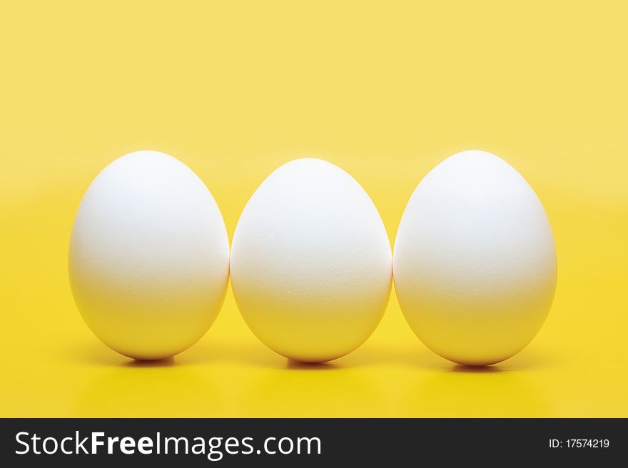 Three white hen's eggs standing vertical on yellow background. Three white hen's eggs standing vertical on yellow background