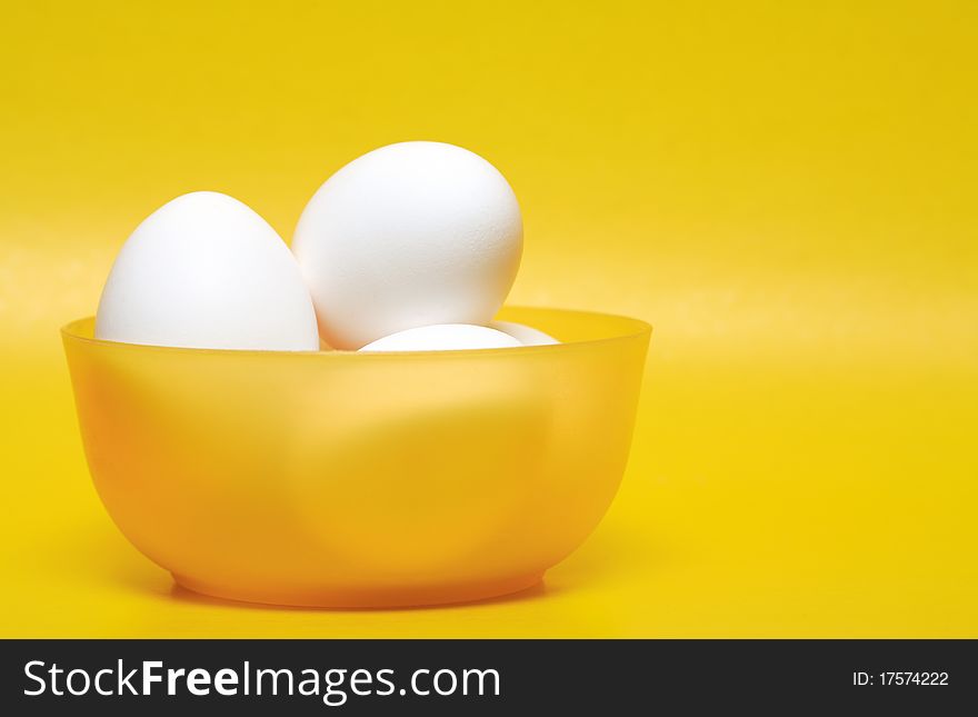 Few white hen's eggs in plastic bowl on yellow background. Few white hen's eggs in plastic bowl on yellow background