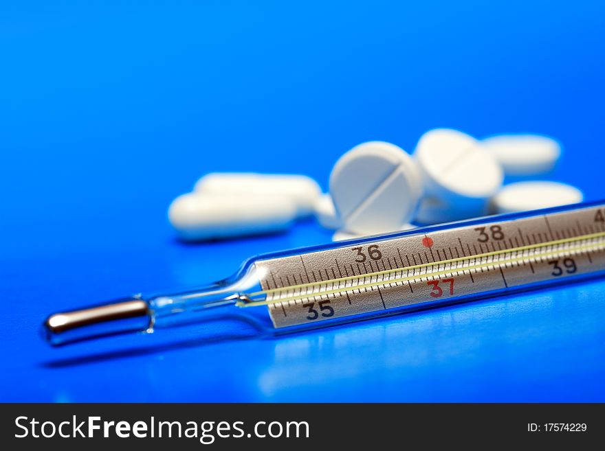 Stack of pills near clinical thermometer on blue background. Stack of pills near clinical thermometer on blue background