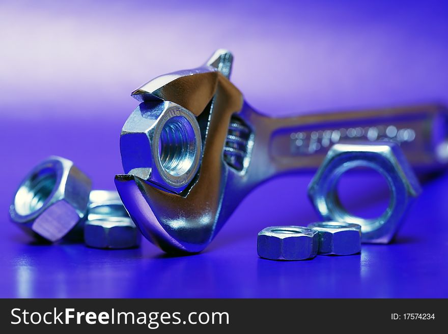 Extreme closeup of adjustable wrench gripping a screw nut on blue background with nuts. Extreme closeup of adjustable wrench gripping a screw nut on blue background with nuts