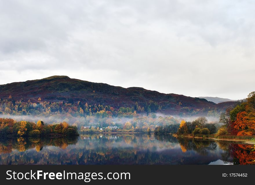 Still water on Grasmere with reflections of Autumn colours and mist. Still water on Grasmere with reflections of Autumn colours and mist