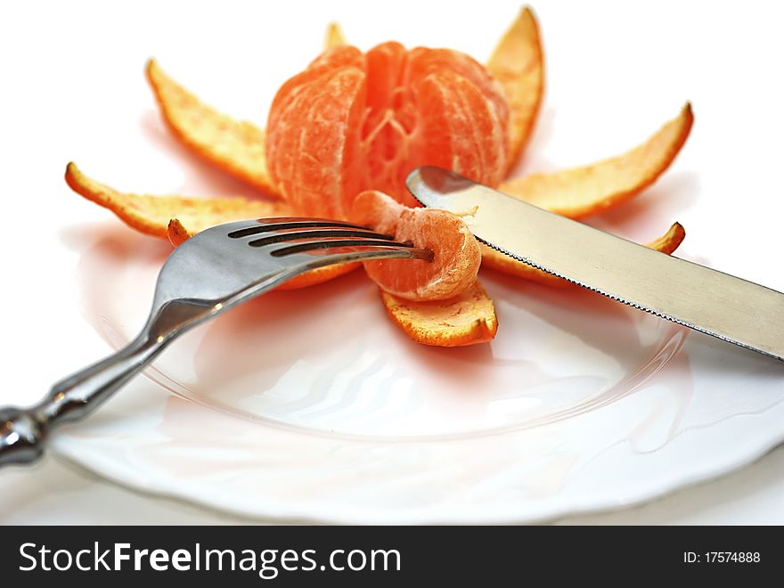 The cleared tangerine on a plate with a plug and a knife on a white background. On a plug the tangerine segment is pinned. The cleared tangerine on a plate with a plug and a knife on a white background. On a plug the tangerine segment is pinned.