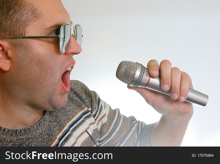 The young man in studio singing in a microphone on a gray background. The young man in studio singing in a microphone on a gray background