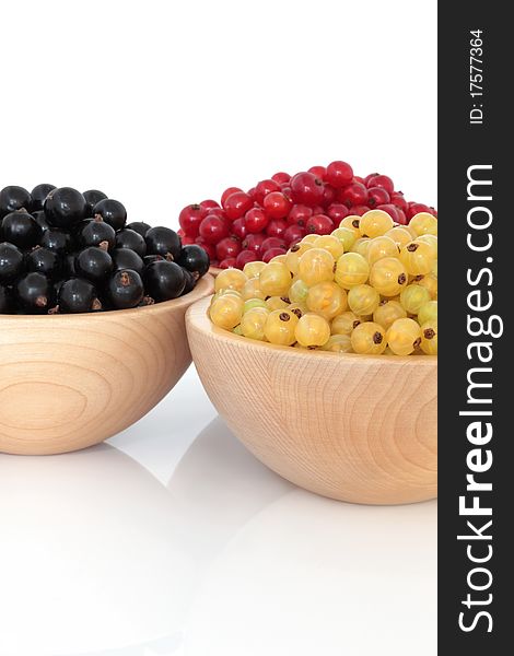 Red, black and white currants in beech wood bowls over white background.