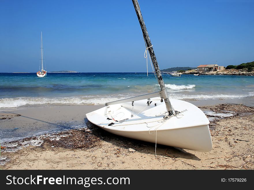 Small white sailing boat on the sand beach with the blue sea and bright blue sky in background. Small white sailing boat on the sand beach with the blue sea and bright blue sky in background.