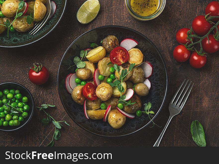 Baby potatoes salad with green peas and radish, black background, top view