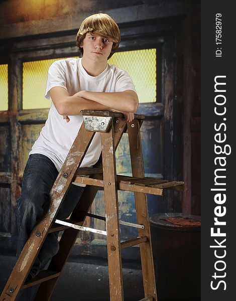 A serious young teen on a ladder inside a grungy, old garage. A serious young teen on a ladder inside a grungy, old garage.