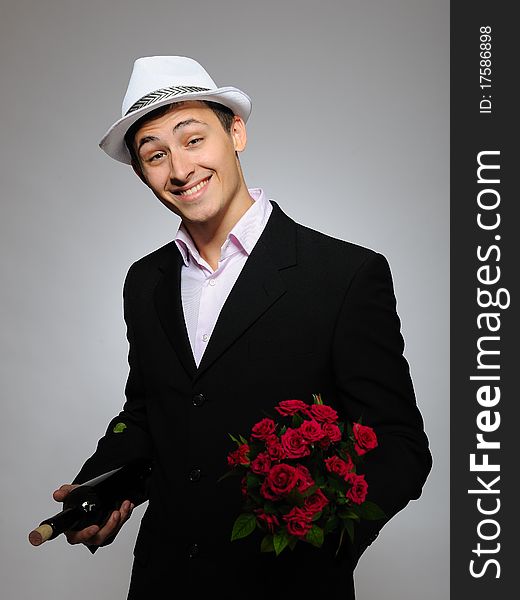 Handsome romantic young man holding rose flower and vine bottle prepared for a date. gray background. Handsome romantic young man holding rose flower and vine bottle prepared for a date. gray background