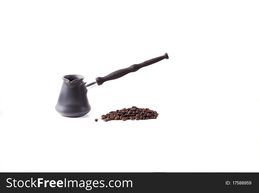 Coffee maker from dark metal with the long wooden handle of dark color and coffee grains fried on a white background. Coffee maker from dark metal with the long wooden handle of dark color and coffee grains fried on a white background