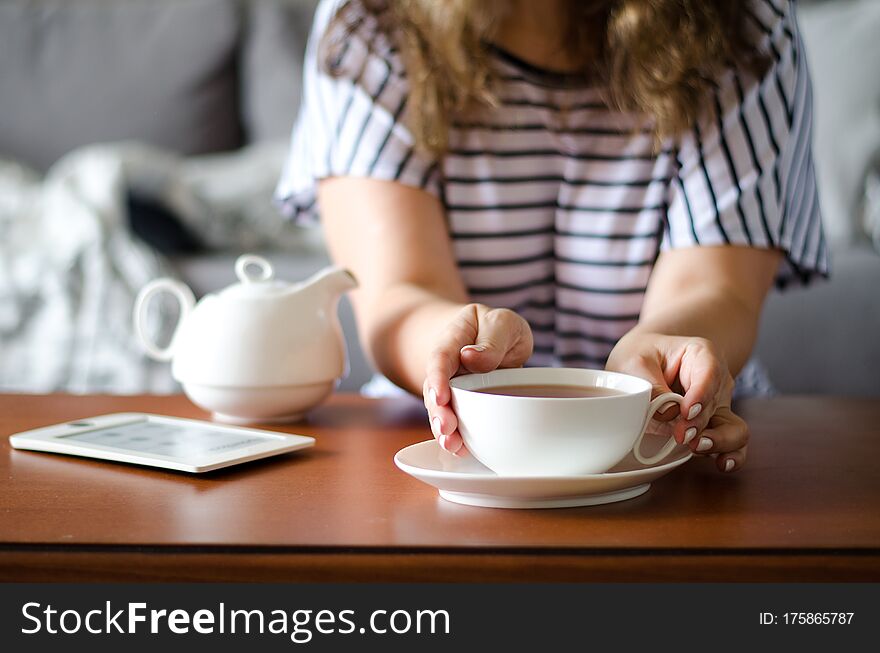 Cozy home interior with teapot, eBook and woman holding cup of tea. Horizontal. Cozy home interior with teapot, eBook and woman holding cup of tea. Horizontal