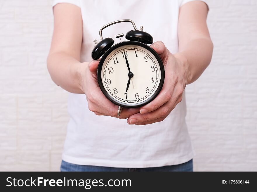 Woman holding an alarm clock in hands, the time is 7 am, early morning waking up.