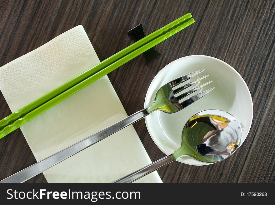Green chopsticks,fork and spoon table setting with napkin on wood table.horizontal image. Green chopsticks,fork and spoon table setting with napkin on wood table.horizontal image