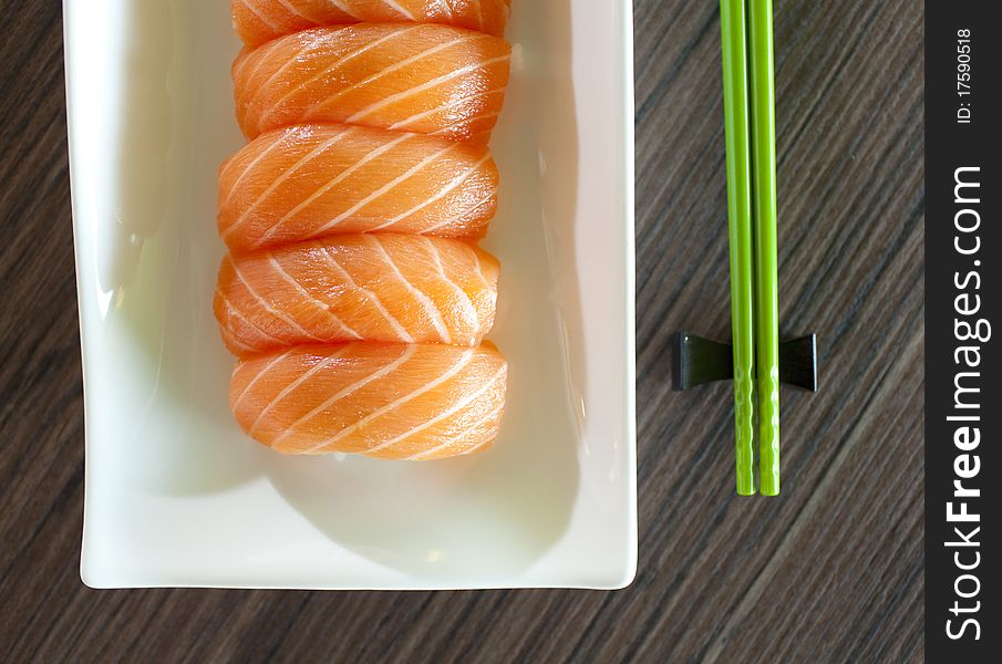 Salmon Sushi on plate with green chopsticks on wood table. Salmon Sushi on plate with green chopsticks on wood table