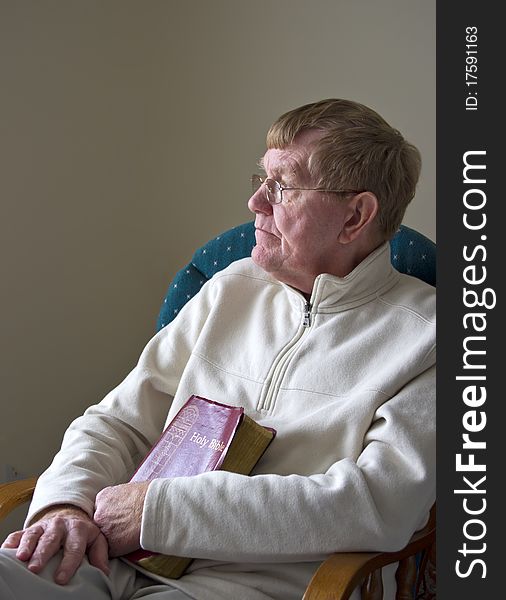 An older man sitting in a chair with his Bible. An older man sitting in a chair with his Bible.