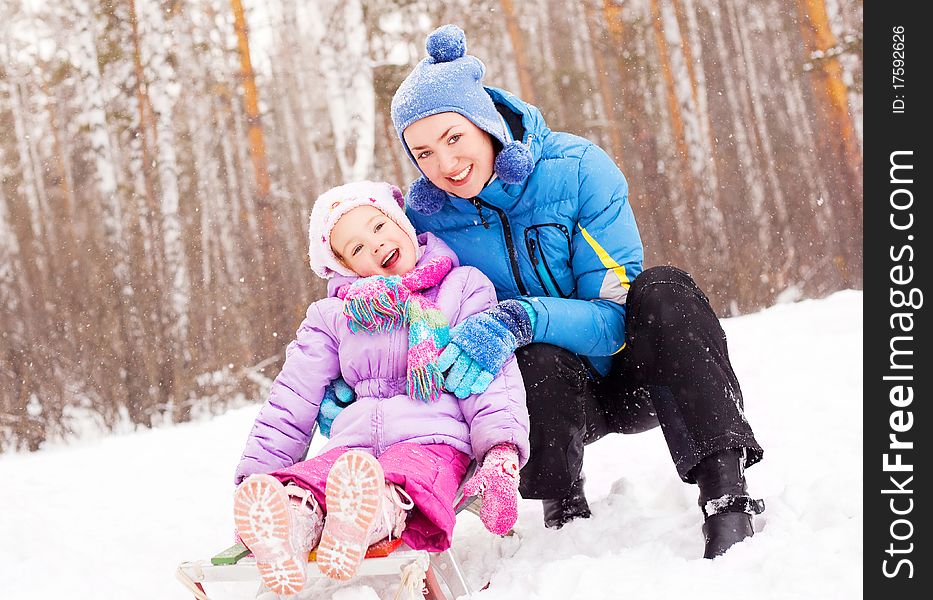 Happy family; young mother and her daughter with a sled having fun in the winter park. Happy family; young mother and her daughter with a sled having fun in the winter park