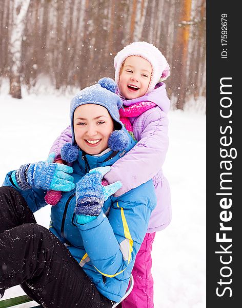 Happy family; young mother and her daughter with a sled having fun in the winter park (focus on the child). Happy family; young mother and her daughter with a sled having fun in the winter park (focus on the child)